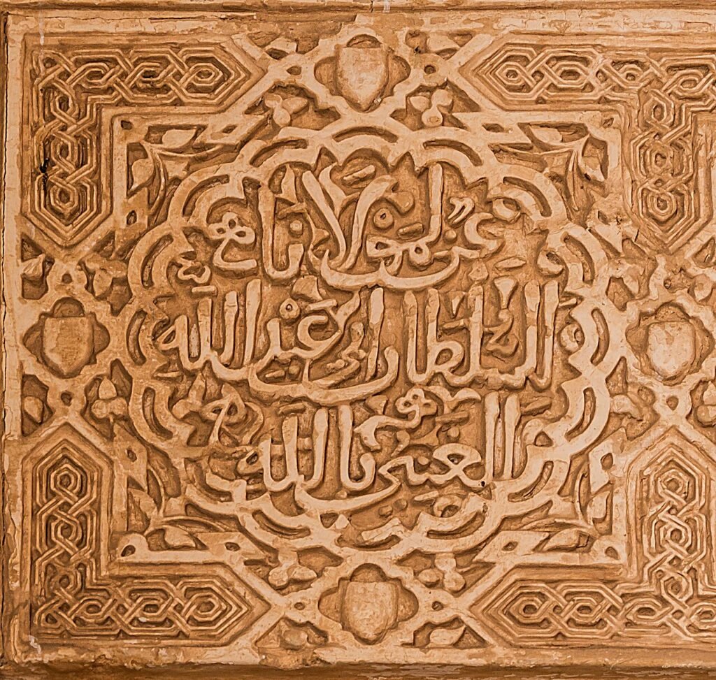 Photo : Jebulon, CC0, Wikimedia Commons Panneau de stuc sculpté de l’Alhambra portant la devise des Nasrides en calligraphie arabe